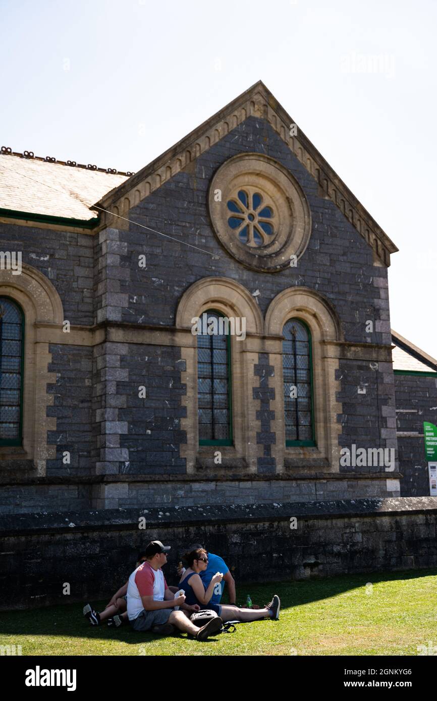 Touristen entspannen sich an der historischen Steinkirche mit normannischer Architektur in Cornwall Stockfoto