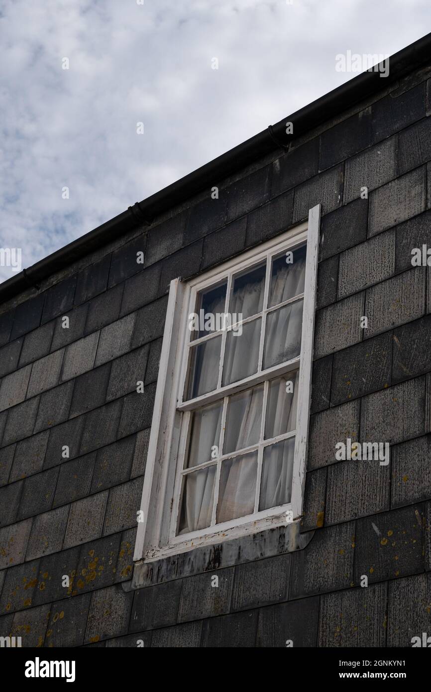 Traditionelles kornisches Cottage mit verwittertem Schieferboden und weißem Schiebefenster vor bewölktem Himmel Stockfoto