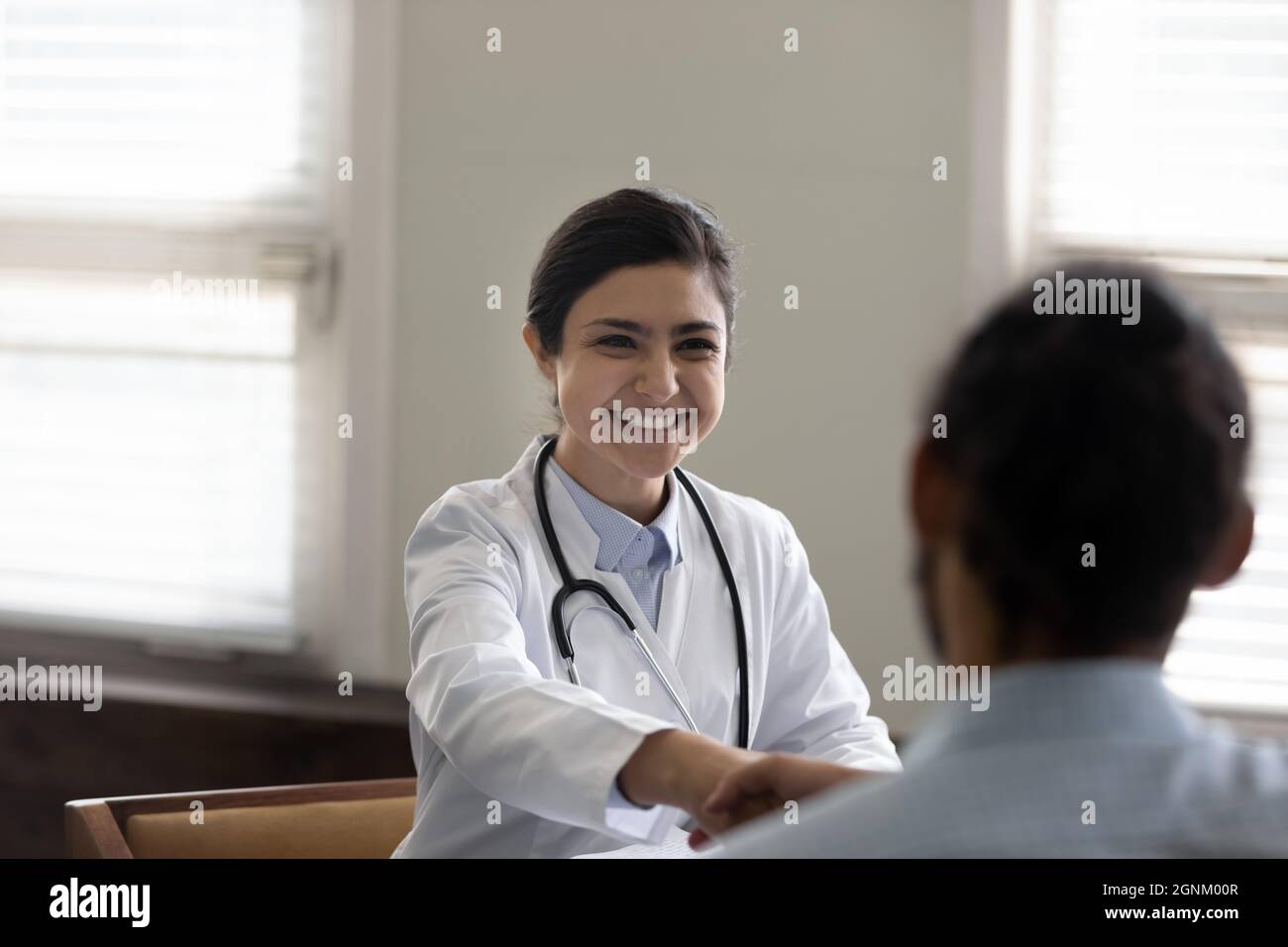 Glücklicher erfolgreicher junger indischer Arzt, der dem Patienten Handschlag gab Stockfoto