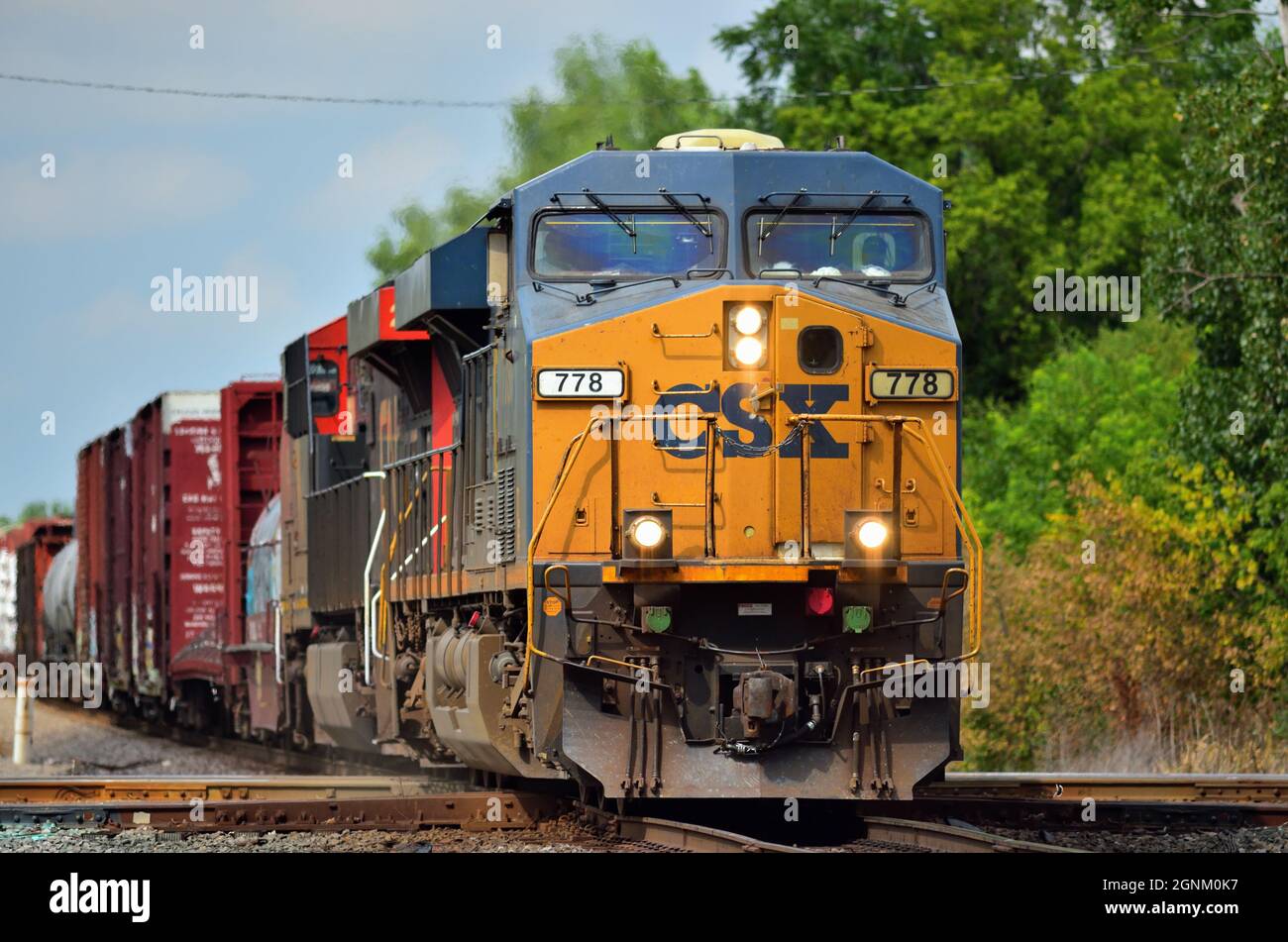 Bartlett, Illinois, USA. Eine Offroad-CSX Transportation-Lokomotive führt einen Güterzug der Canadian National Railway durch eine Kreuzung. Stockfoto