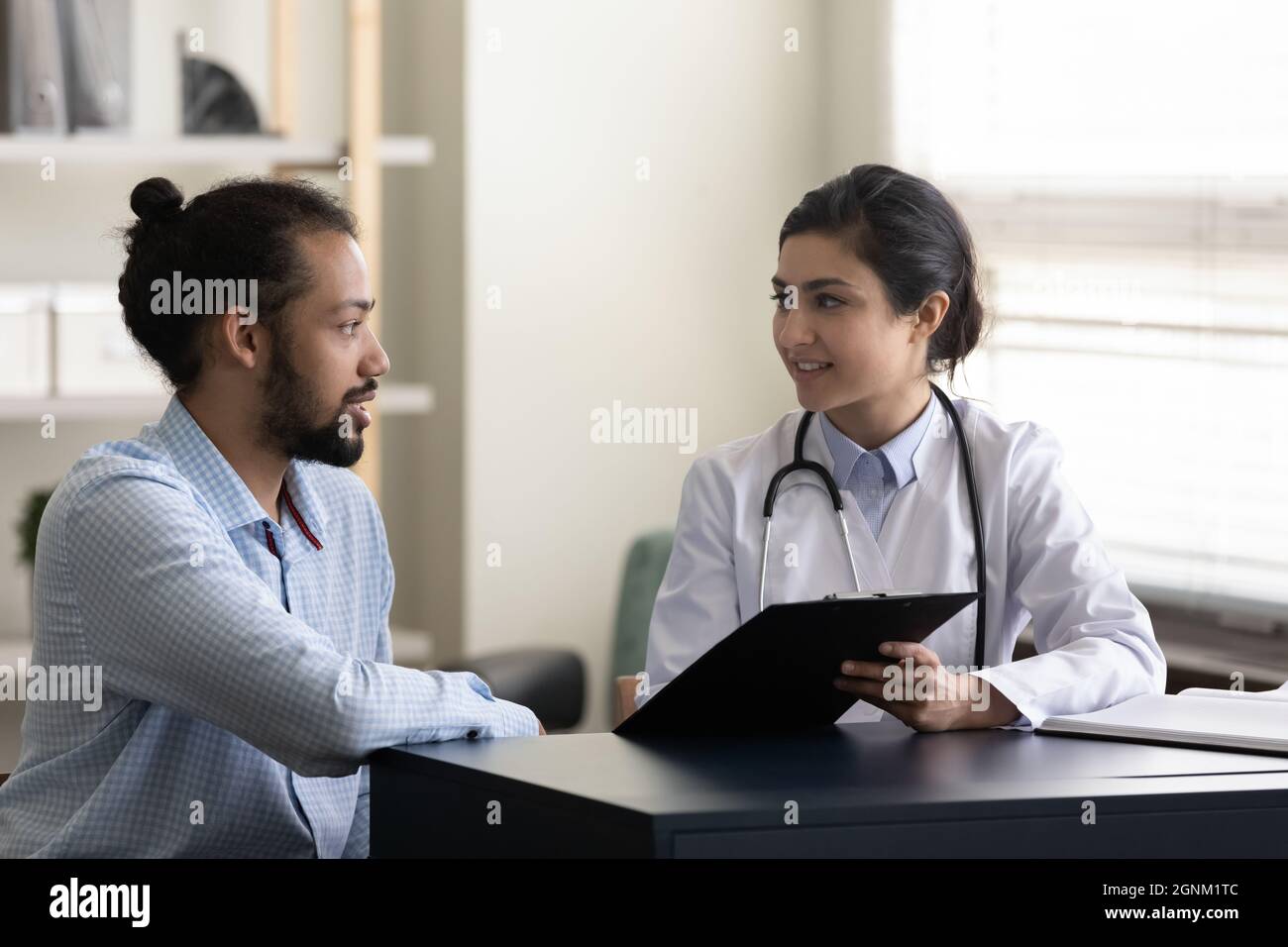Junger indischer Hausarzt zeigt dem männlichen Patienten eine Unterlage Stockfoto