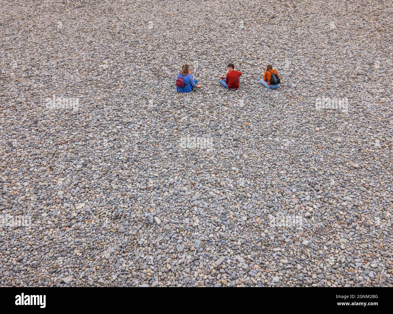 Drei Teenager sitzen an einem Kiesstrand in Wales Stockfoto