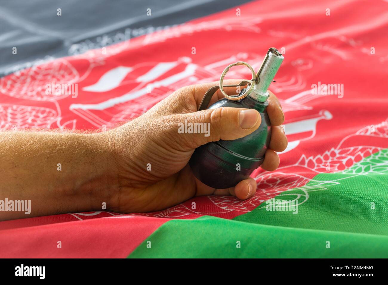 Eine Hand, die eine Granate in der Hand hält, die auf der Flagge Afghanistans liegt, das Konzept des Konflikts und die Bedrohungen des Fundamentalismus Stockfoto