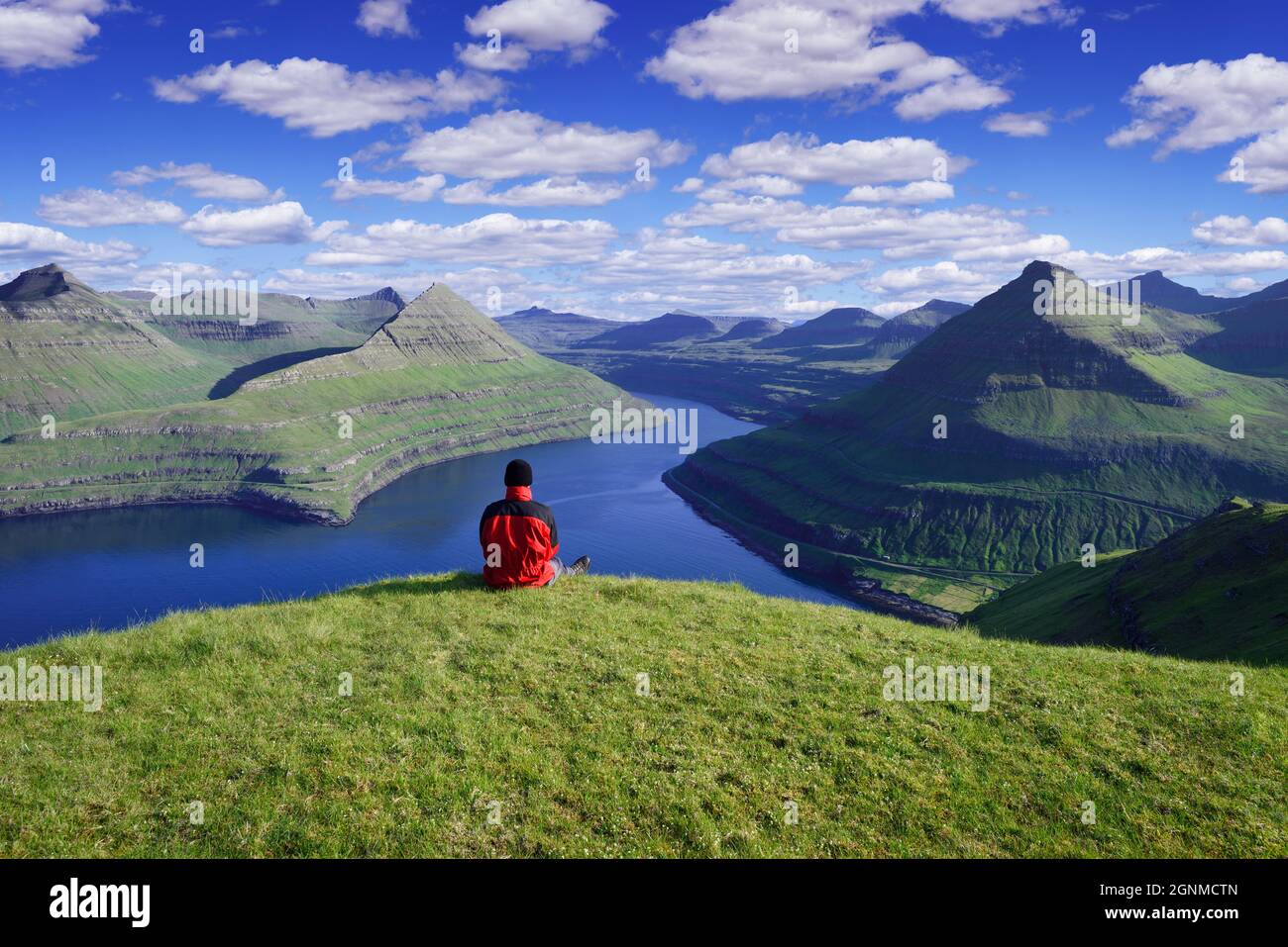 Funningur Fjordansicht und Berge auf Eysturoy Island, Färöer Inseln. Ein Tourist in einer roten Jacke genießt an einem sonnigen Tag die wunderschöne nördliche Landschaft Stockfoto