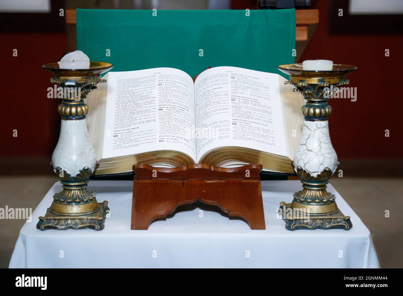 Die Heilige Bibel öffnet sich auf einem Holzaltar und einem Kerzenständer an der Seite Stockfoto