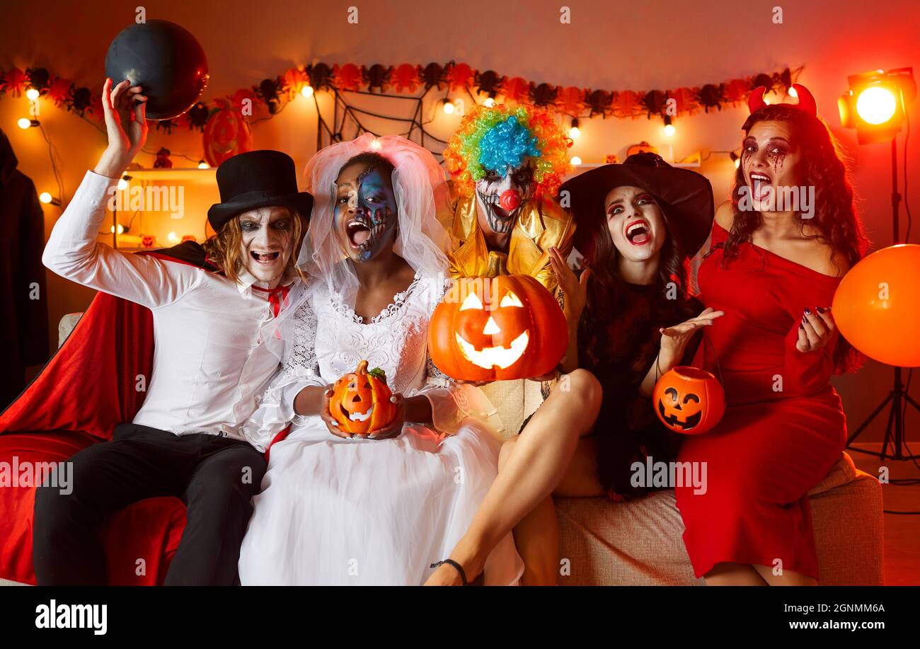Eine Gruppe von Menschen in Halloween-Kostümen sitzt auf der Couch und schreit auf einer lustigen Party zu Hause Stockfoto