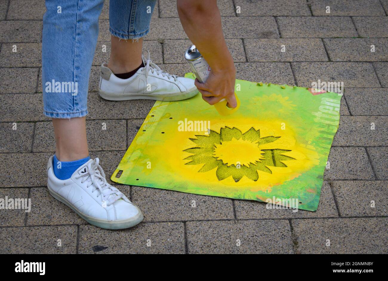 Potsdam, Deutschland. September 2021. Ein Kampagnenmitarbeiter für Bündnis  90/die Grünen sprüht mit einer Schablone aus Karton und gelbem Farbspray  die Blüte einer Sonnenblume auf den Bürgersteig. Quelle: Soeren  Stache/dpa-Zentralbild/dpa/Alamy Live ...