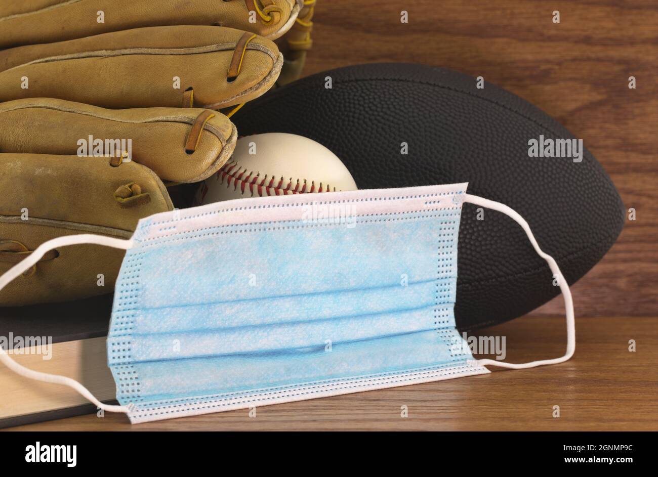 Schwarzer Fußball, abgenutzter Baseballhandschuh und Ball, Buch und persönliche Schutzmaske spiegeln die Empfehlungen der Schule Covid-19 für die öffentliche Gesundheit und wider Stockfoto