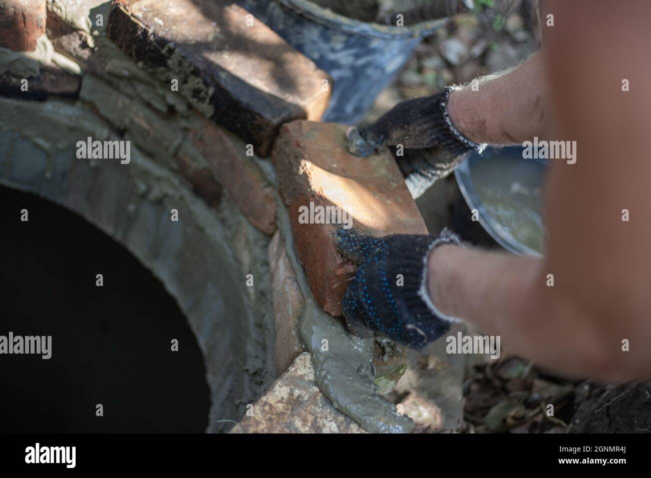 Ein Arbeiter legt den Mund eines septischen Brunnenes aus Ziegelsteinen. Mit Zement arbeiten. Stockfoto