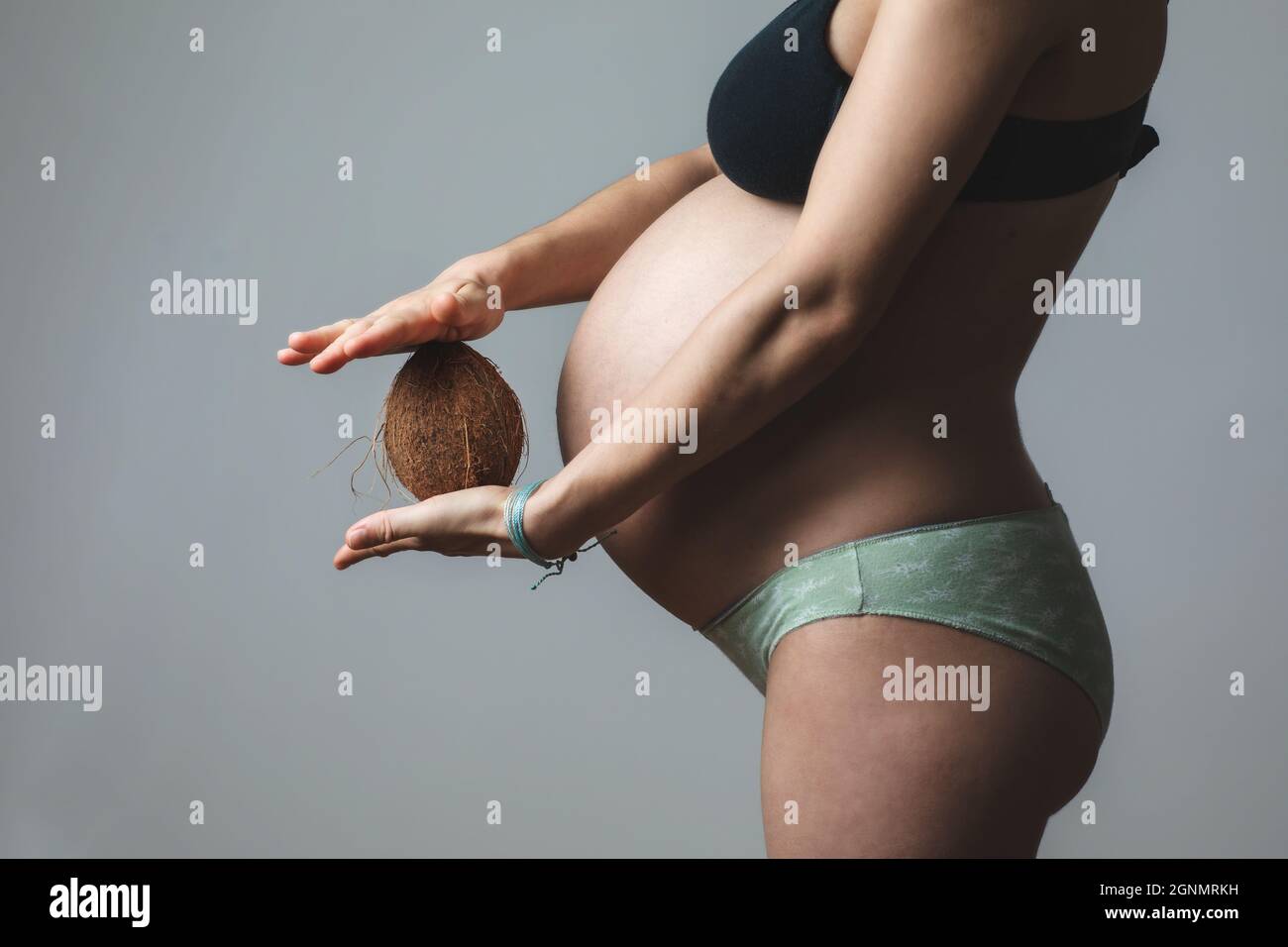 Schwanger Weibchen hält Kokosnuss vor dem Bauch. Stockfoto