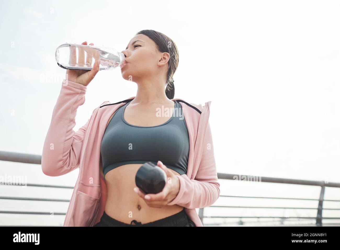 Junge sportliche Frau, die nach dem Sporttraining im Freien Wasser aus der Flasche trinkt Stockfoto