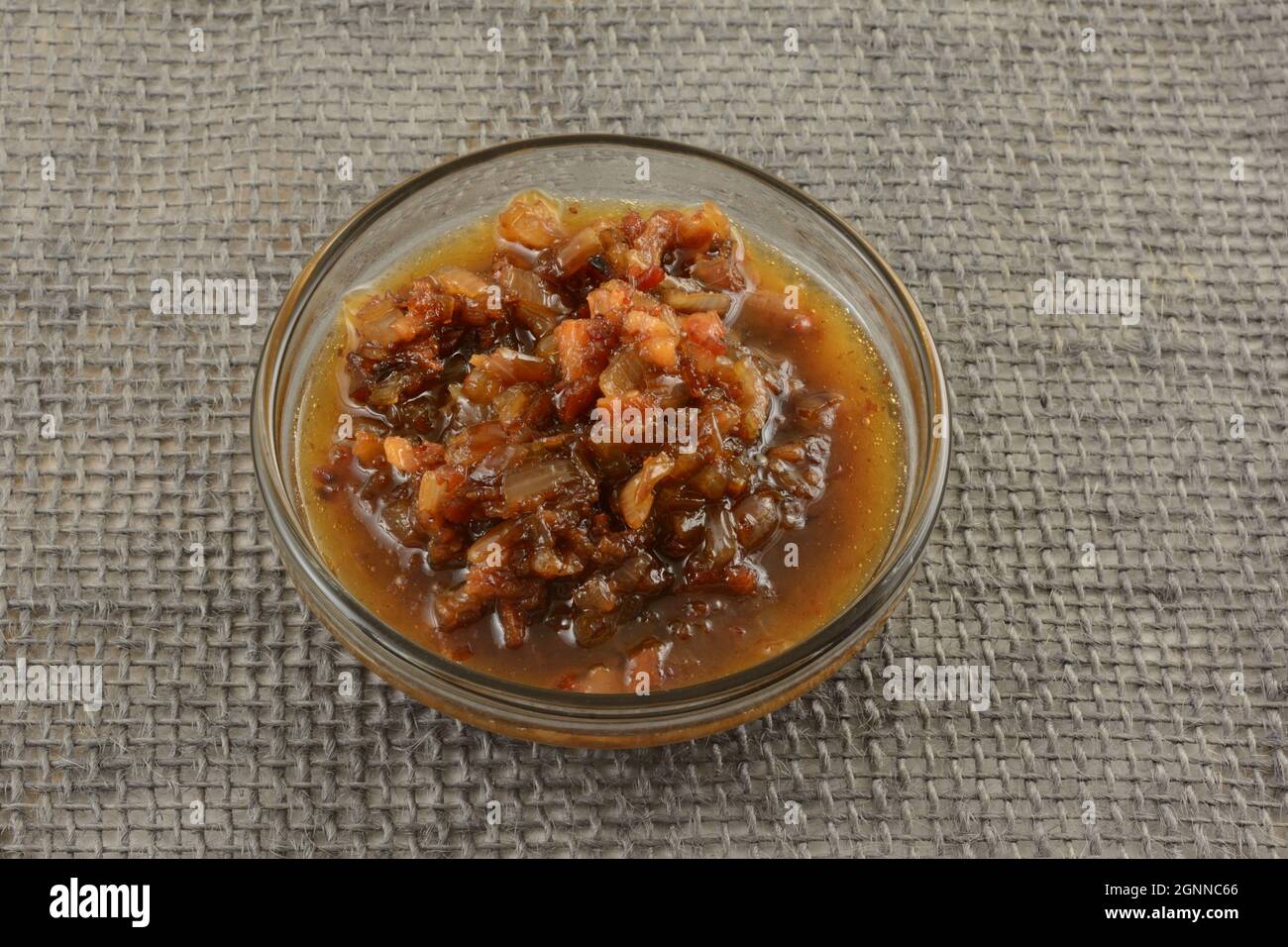 Rotwein-Sauce mit Speck und gehackter Schalotte auf Glaszutat-Schüssel auf grauem Sackleinen Stockfoto