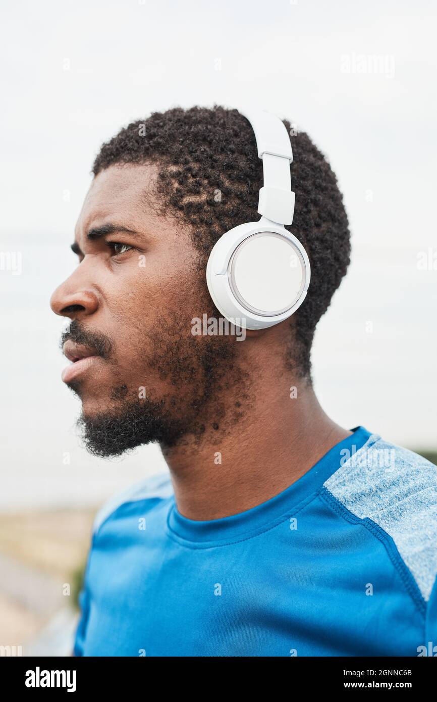 Afrikanischer junger Sportler mit kabellosen Kopfhörern, der im Freien Musik hört Stockfoto