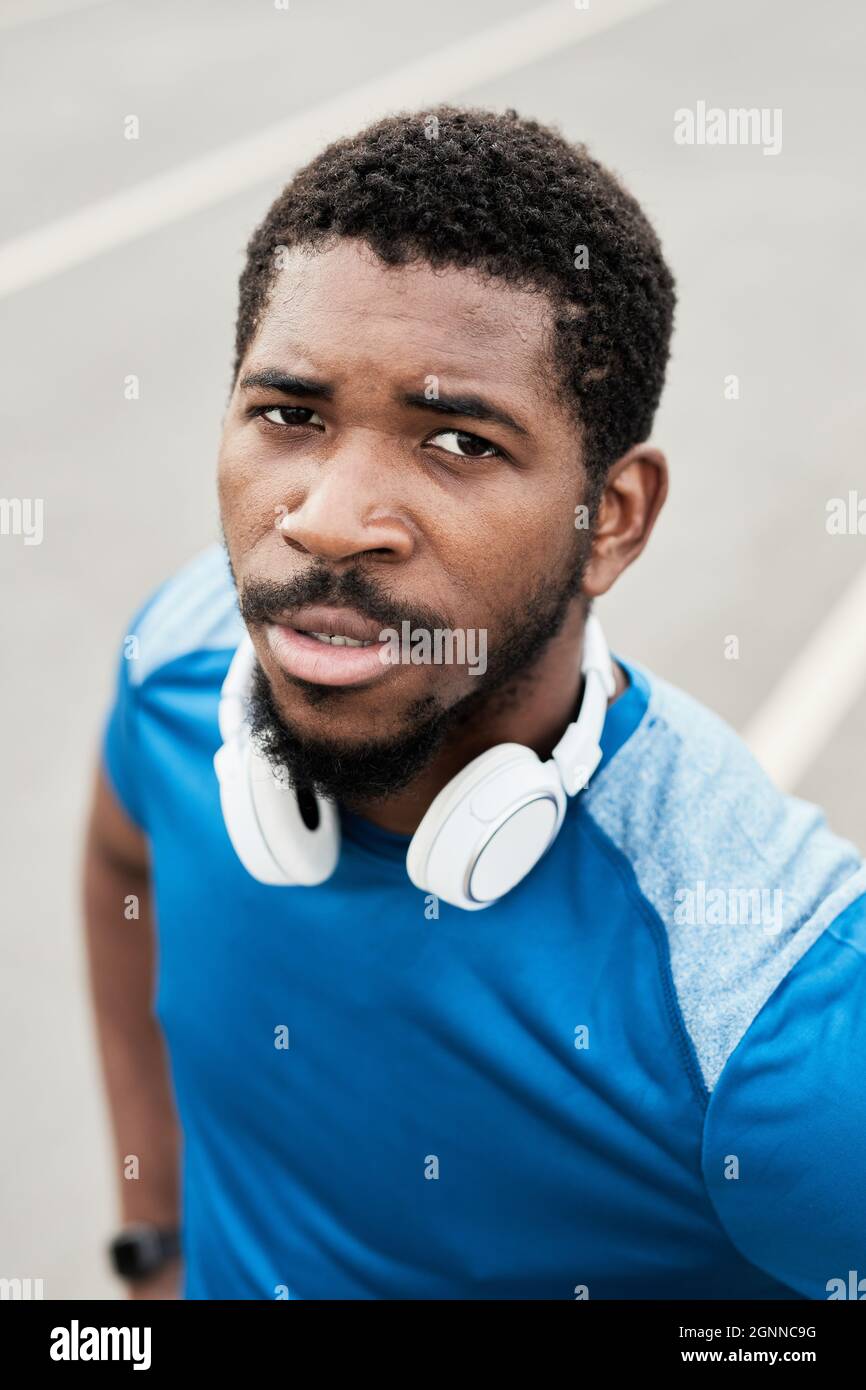 Porträt eines jungen afrikanischen Läufers in kabellosen Kopfhörern, der während des Laufens in der Stadt die Kamera anschaut Stockfoto