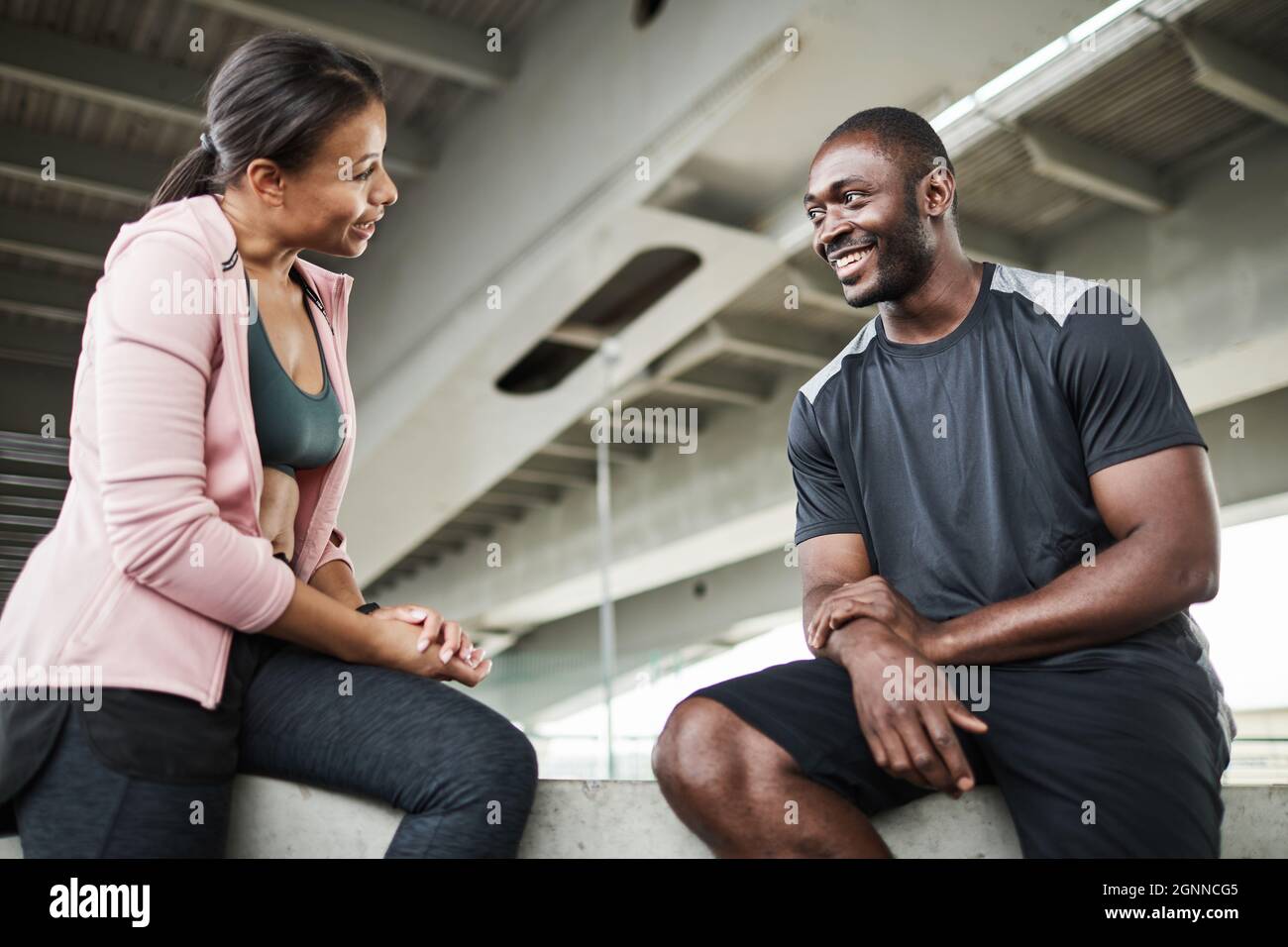 Afrikanische junge Frau diskutiert mit ihrem Trainer über Sporttraining, während sie im Fitnessstudio sitzt Stockfoto