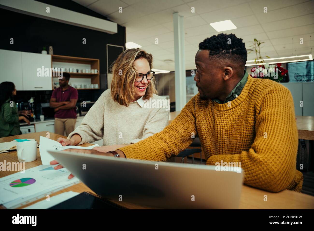 Geschäftsfrau lacht und Mann, während sie Informationen auf einem Laptop recherchiert und im Büro über Dokumente diskutiert Stockfoto
