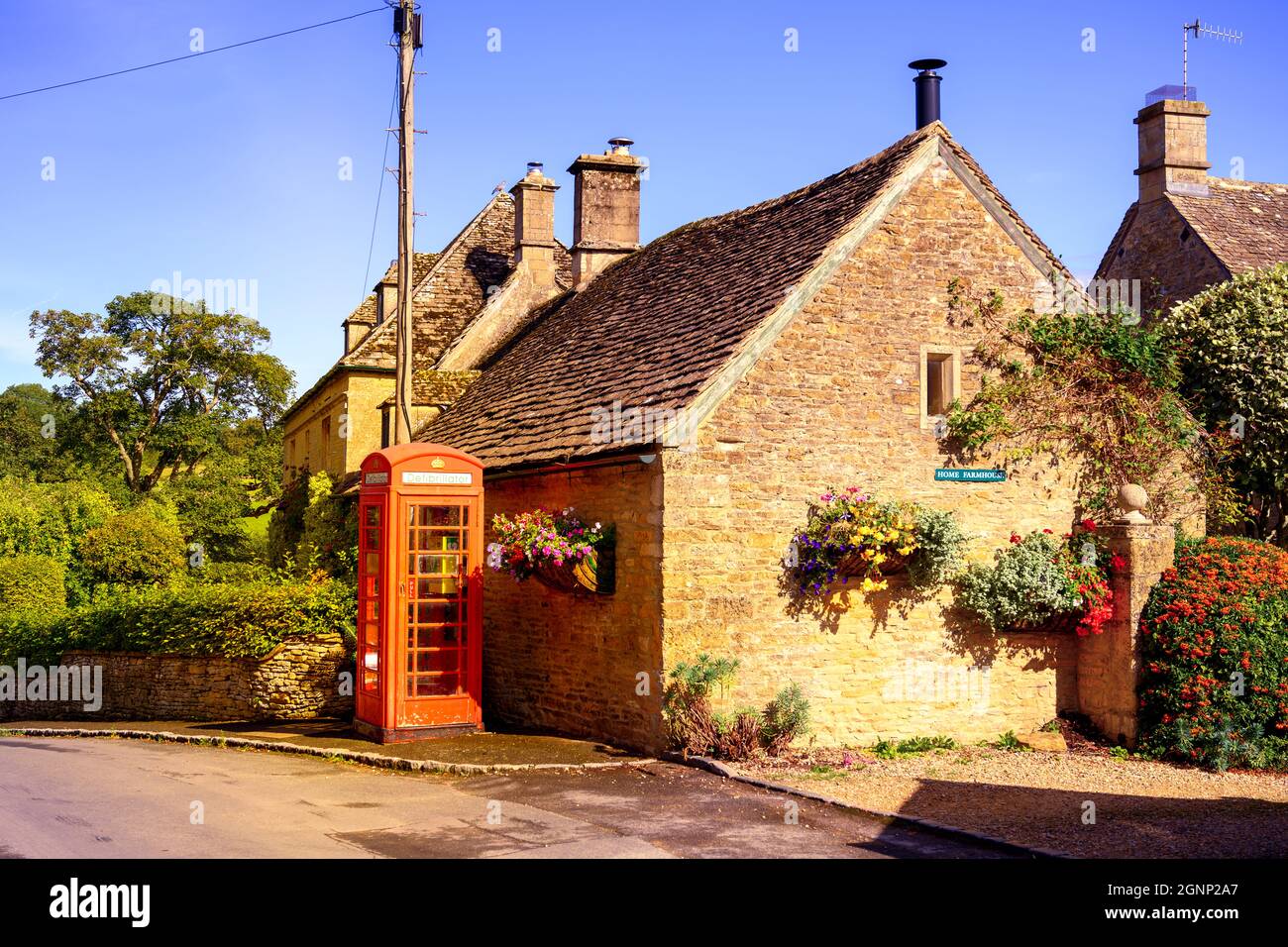 Traditionelle rote Telefonbox vor einem aus Stein gebauten Cotswold Cottage, das jetzt als Defibrillator-Lagerstation genutzt wird. Upper Slaughter Gloucestershire England Großbritannien Stockfoto