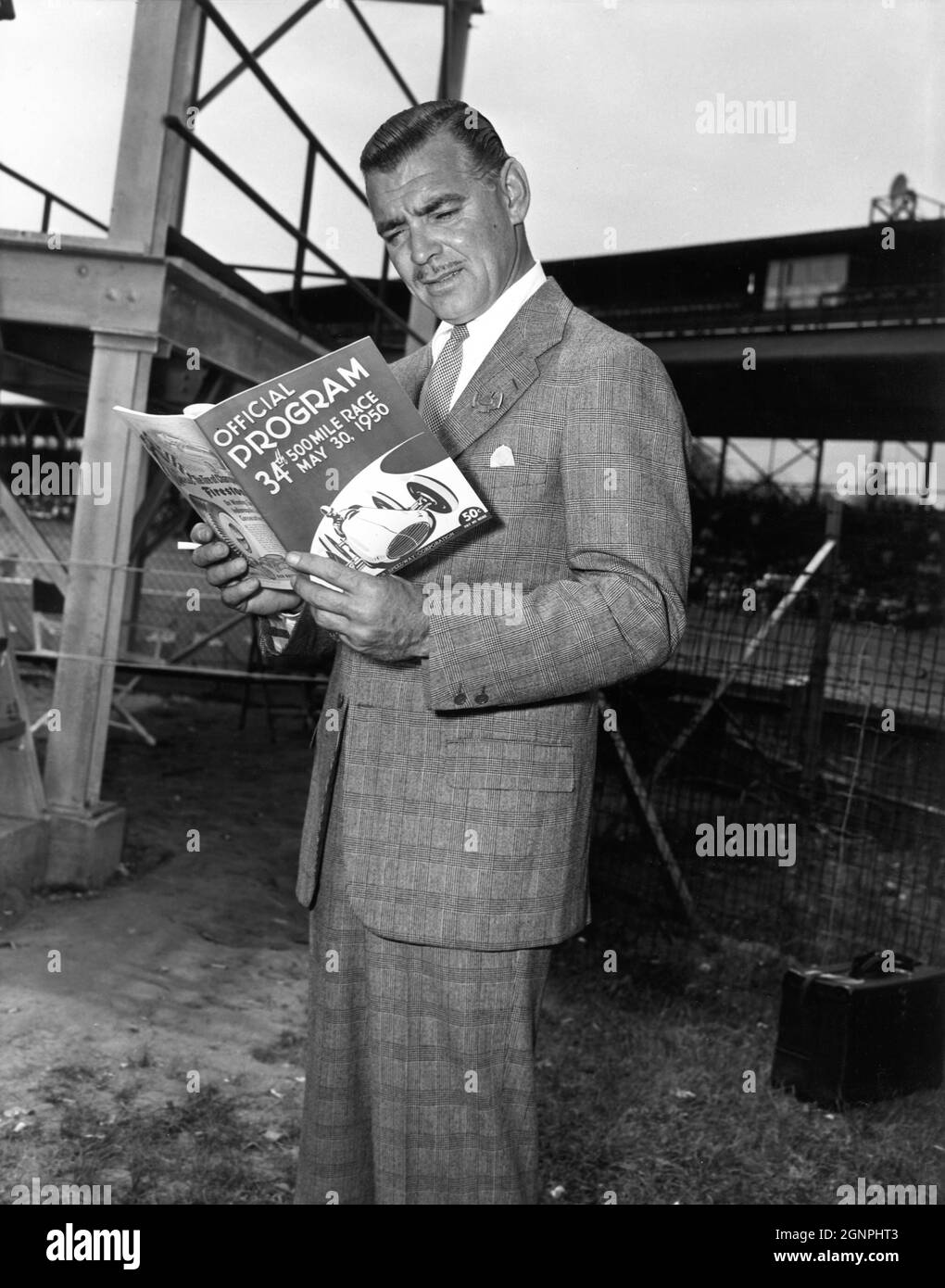 CLARK GABLE an der Drehort-Location studierte offen das offizielle Programm des Indianapolis Motor Speedway Race 1950, wo Szenen für seinen neuesten Film „TO PLEASE A LADY“ (1950) gedreht wurden, Regisseur CLARENCE BROWN Story / Drehbuch Barré Lyndon und Marge Decker Kostümdesign Helen Rose Metro Goldwyn Mayer Stockfoto