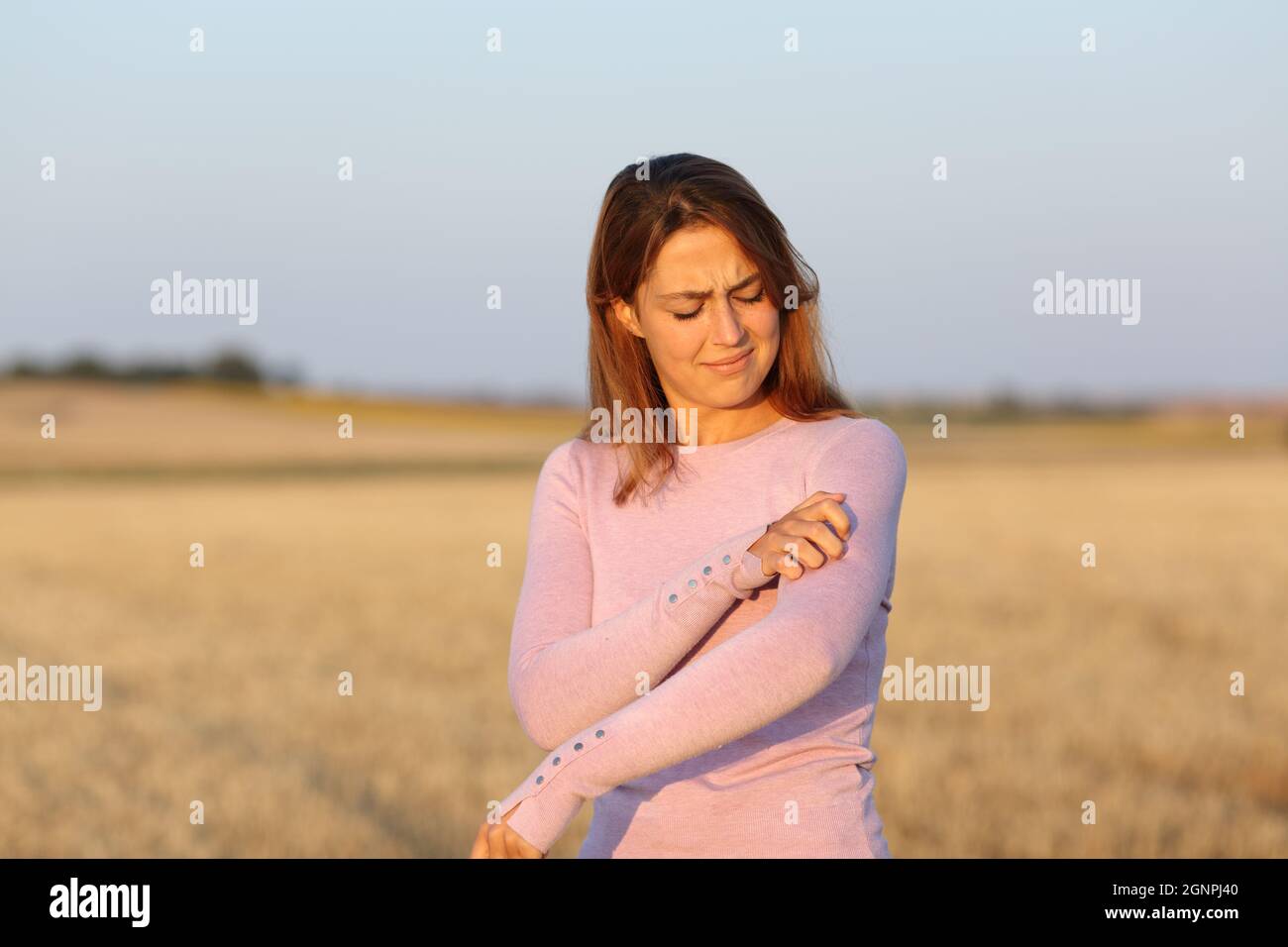 Gestresste Frau kratzt juckenden Arm auf einem geernteten Feld Stockfoto