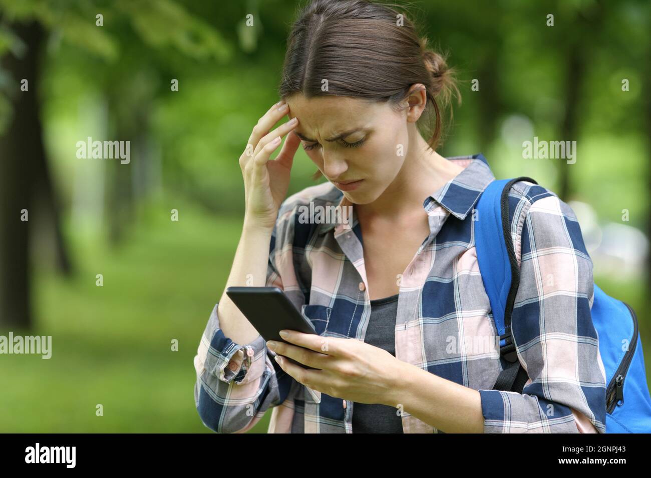 Besorgter Student, der Smartphone in einem Park überprüft Stockfoto