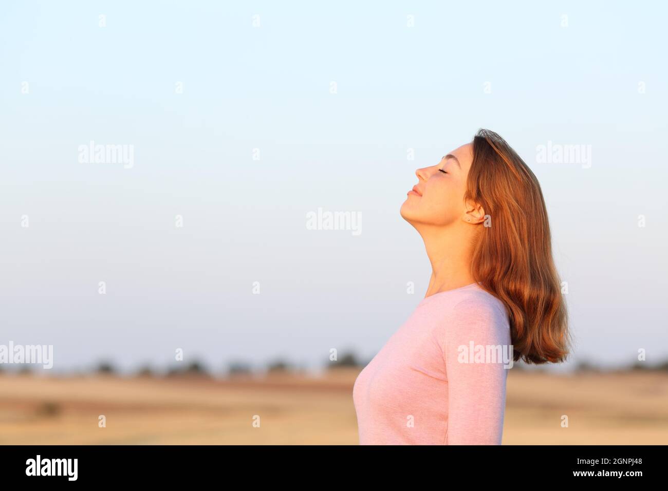 Seitenansicht Porträt einer entspannten Frau, die bei Sonnenaufgang auf einem Feld frische Luft atmet Stockfoto