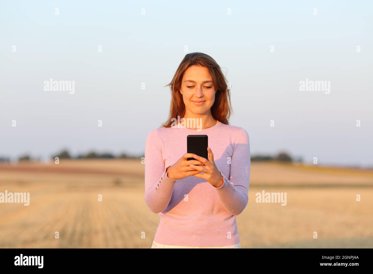 Vorderansicht einer glücklichen Frau, die Smartphone auf geerntetem Feld benutzt Stockfoto
