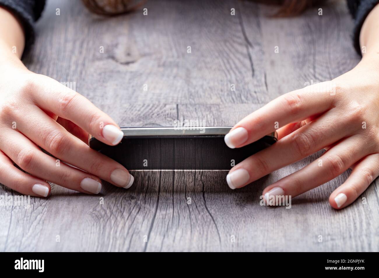 Smartphone horizontal von zwei weiblichen Händen auf einem großen Holzregal unterstützt, haben die gepflegten Hände die französische Maniküre Stockfoto