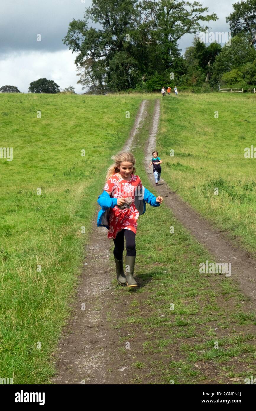 Kinder glückliches Mädchen, das im Sommer im Dinefwr Park Llandeilo Carmarthenshire Wales UK auf einer ländlichen Strecke auf einem Familienspaziergang läuft. KATHY DEWITT 2021 Stockfoto