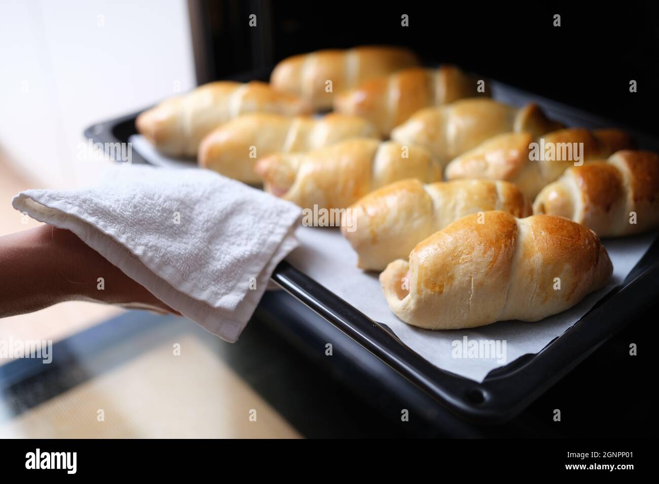 Hausfrau nimmt heiße leckere Brötchen aus dem Ofen auf Backblech Nahaufnahme Stockfoto
