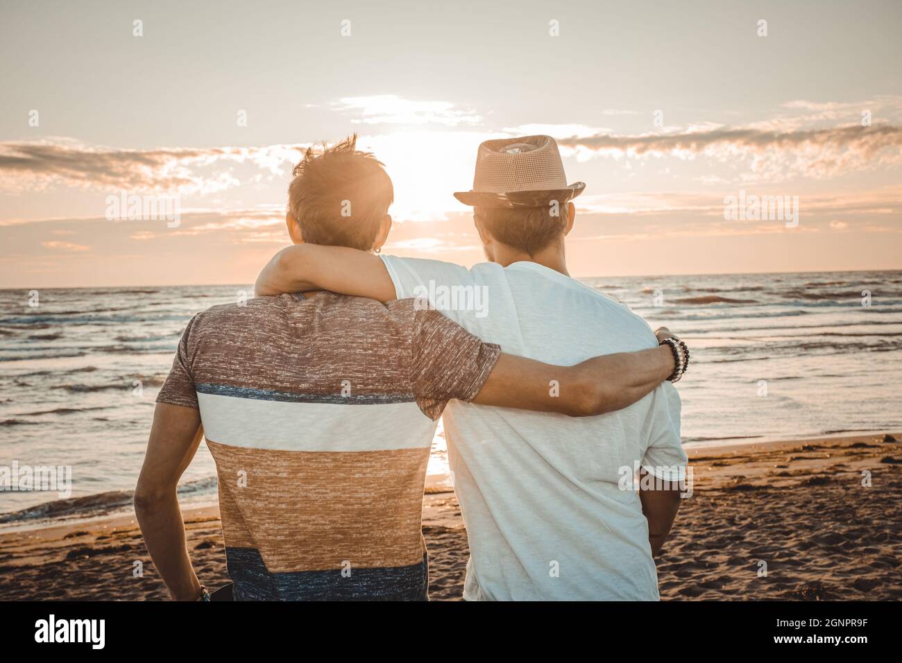 Zwei Freunde umarmen sich gegenseitig und schauen sich den Sonnenuntergang am Strand an. Freundschaft und Liebeskonzept Stockfoto