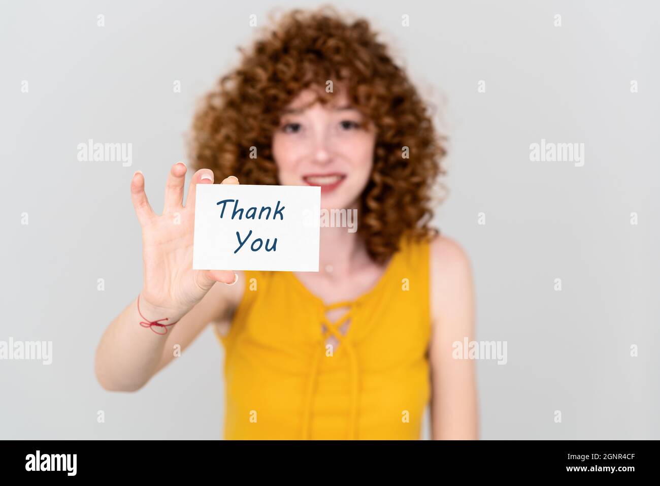 Eine junge Frau mit rotem Haar hält ein Papier mit einer Dankesnote. Geräuschloses Kommunikationskonzept. Hochwertige Fotos Stockfoto