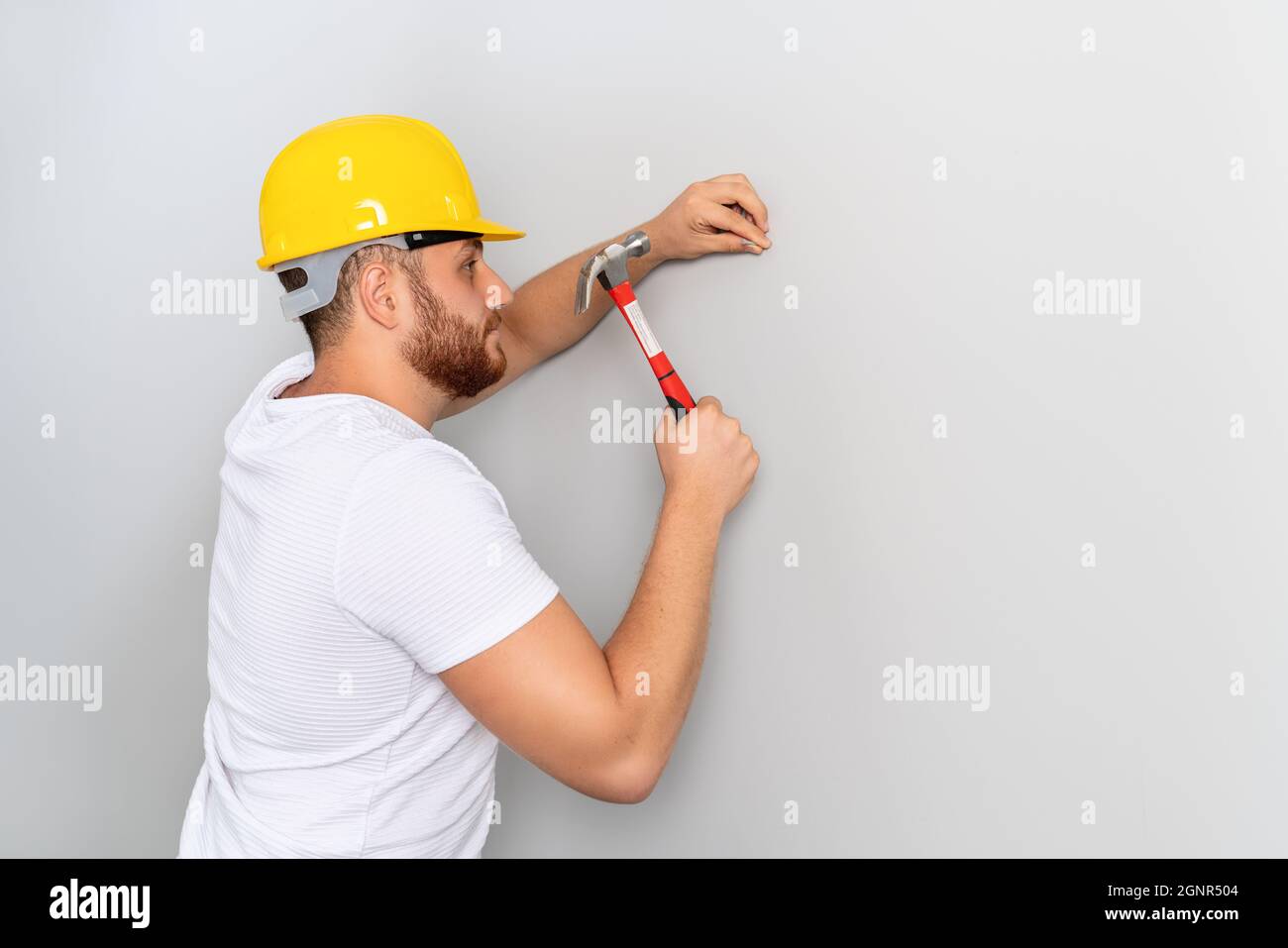Ein junger Arbeiter trifft den Hammer, um ihn für Bauarbeiten oder Renovierungen an die Wand zu nageln. Hochwertige Fotos Stockfoto