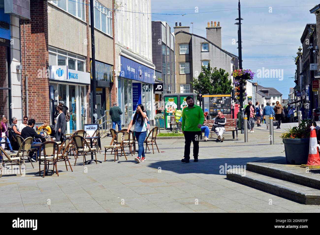 BANGOR, GWYNEDD, WALES. 06-26-21. Hight Street im Stadtzentrum. Menschen saßen an Pflastertischen am Uhrenturm. Stockfoto