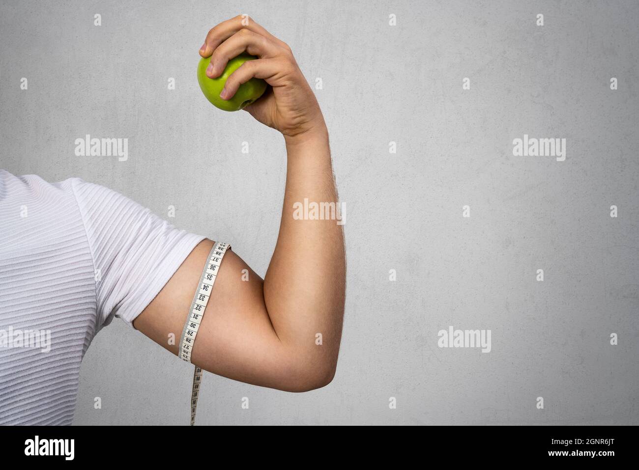 Der junge, athletische Mann hält einen Apfel und zeigt seinen Bizeps. Sport und Ernährung für ein gesundes Leben. Hochwertige Fotos Stockfoto