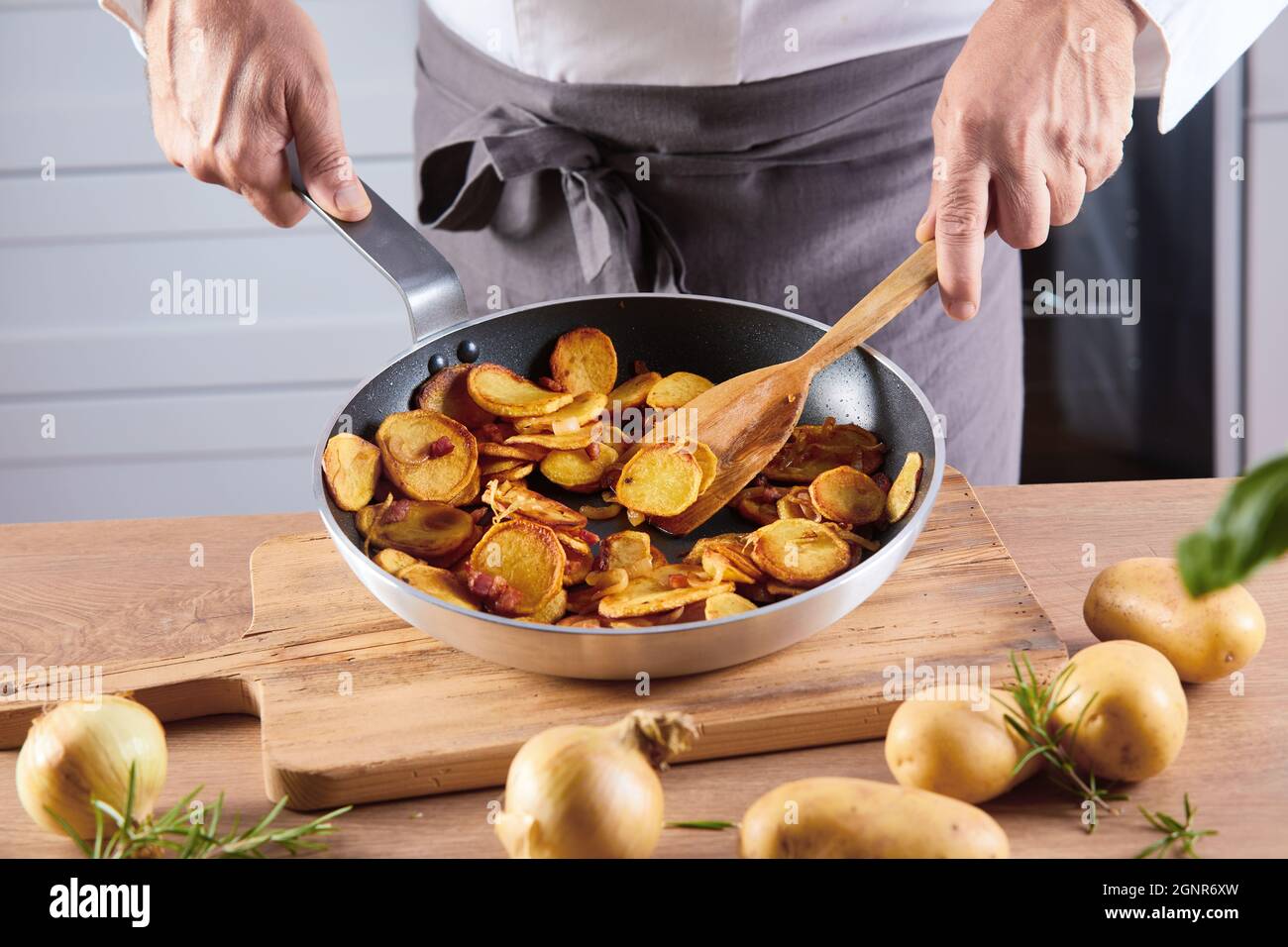Männlicher Koch, der eine Pfanne gebratener Kartoffeln mit ...