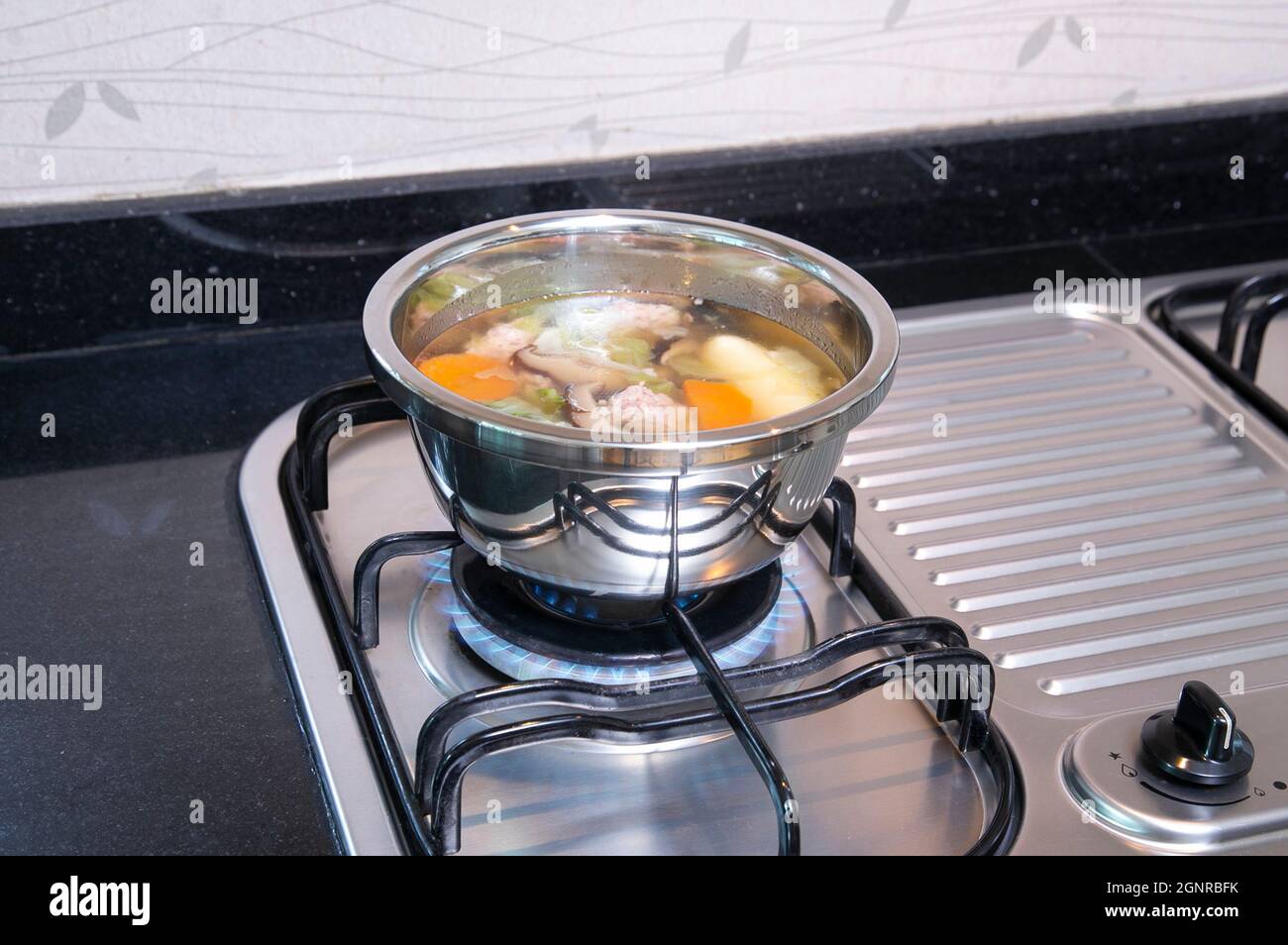 Edelstahlpfanne mit Suppe auf dem Gasherd in der Küche Stockfoto