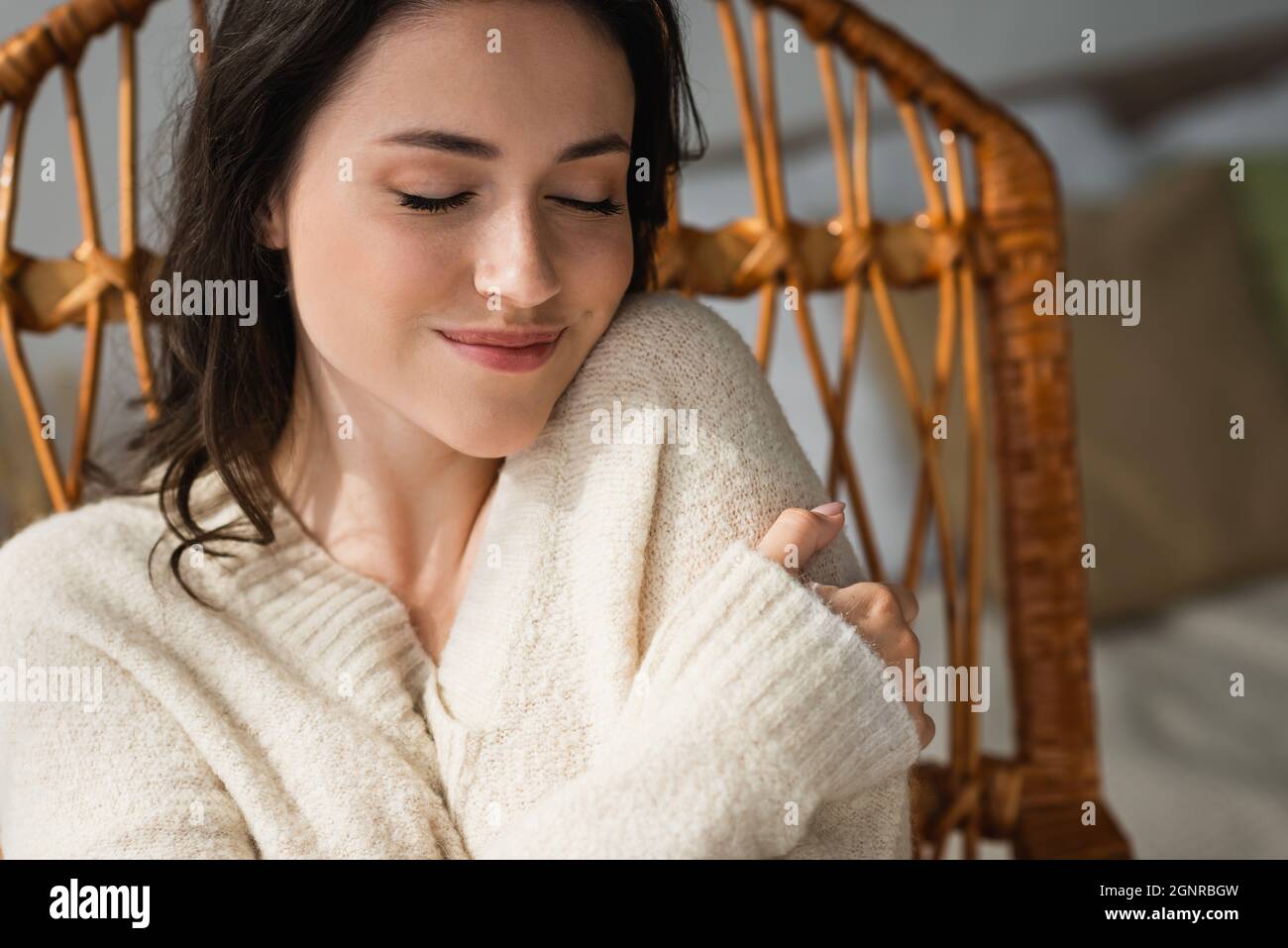 Erfreut Frau in warmen Pullover umarmt sich, während zu Hause mit geschlossenen Augen ruhen Stockfoto