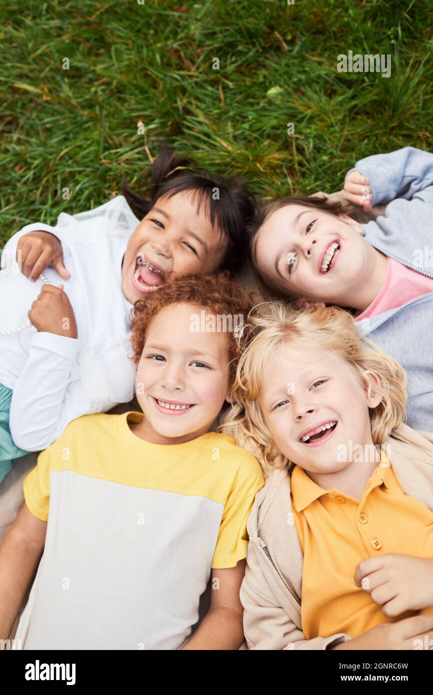Vertikale Draufsicht Porträt einer vielfältigen Gruppe von Kindern, die im Park auf Gras liegen und lächelnd auf die Kamera blicken Stockfoto
