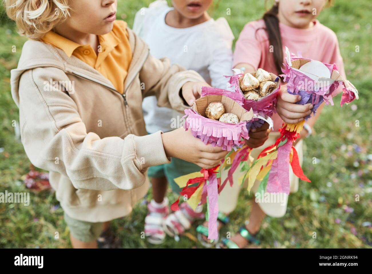 Nahaufnahme von Kindern, die während der Geburtstagsfeier im Freien Süßigkeiten von Pinata halten, Platz kopieren Stockfoto