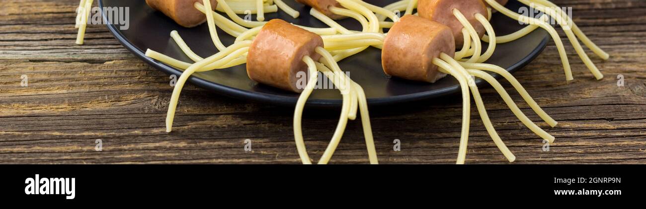 Spaghetti-Banner mit Würsten in Form von Spinnen. Happy Kid Food für Halloween-Party auf Holzhintergrund Stockfoto