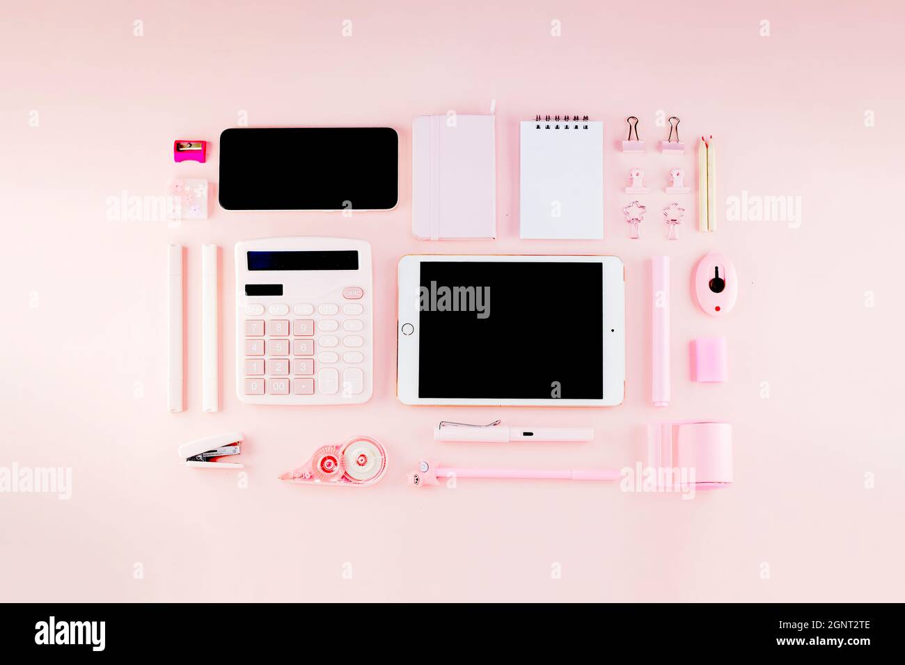 Draufsicht auf den femininen, weichen, pastellfarbenen, pinkfarbenen Desktop-Arbeitsplatz, der aus Taschenrechner, Notizbuch, Stiften, Telefon, Pad, Hefter A Stockfoto