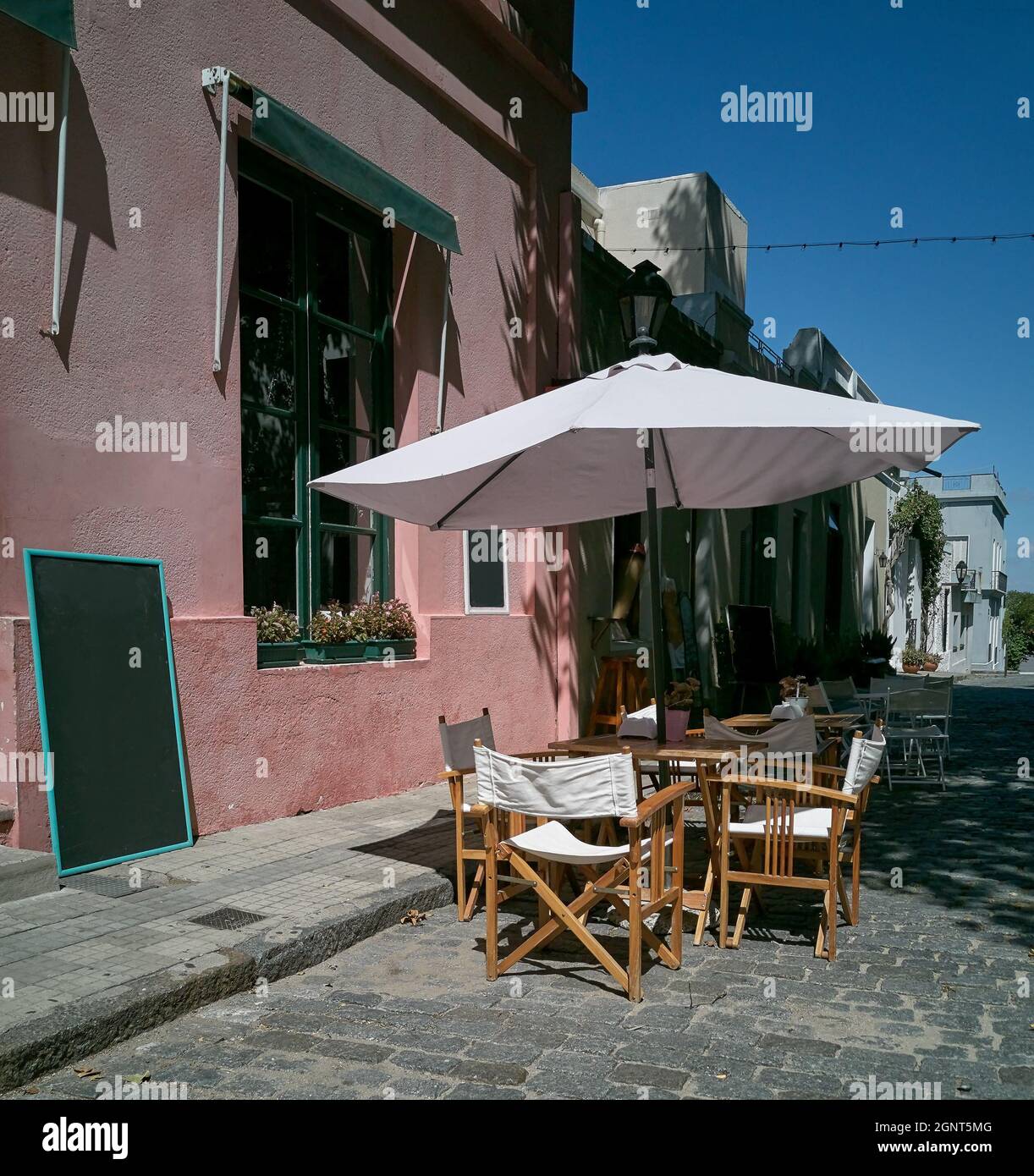 Leerer Tisch in einem Restaurant im Freien in der Altstadt von Colonia Uruguay sind die Tische mit Sonnenschirmen beschattet. Die Straße ist mit altem Kopfsteinpflaster gepflastert Stockfoto