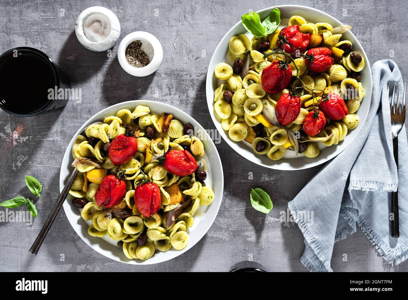 Olecchiette Pasta mit Pesto und gebackenen Kirschtomaten auf dem Steinhintergrund mit Rotwein in den Gläsern Stockfoto