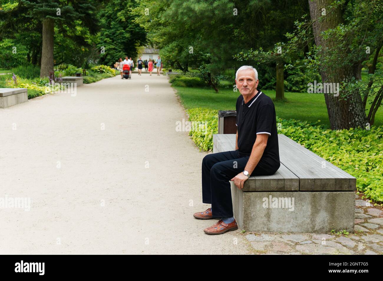 Ganzkörperansicht eines älteren Mannes, der auf einer Parkbank sitzt und die Kamera anschaut Stockfoto