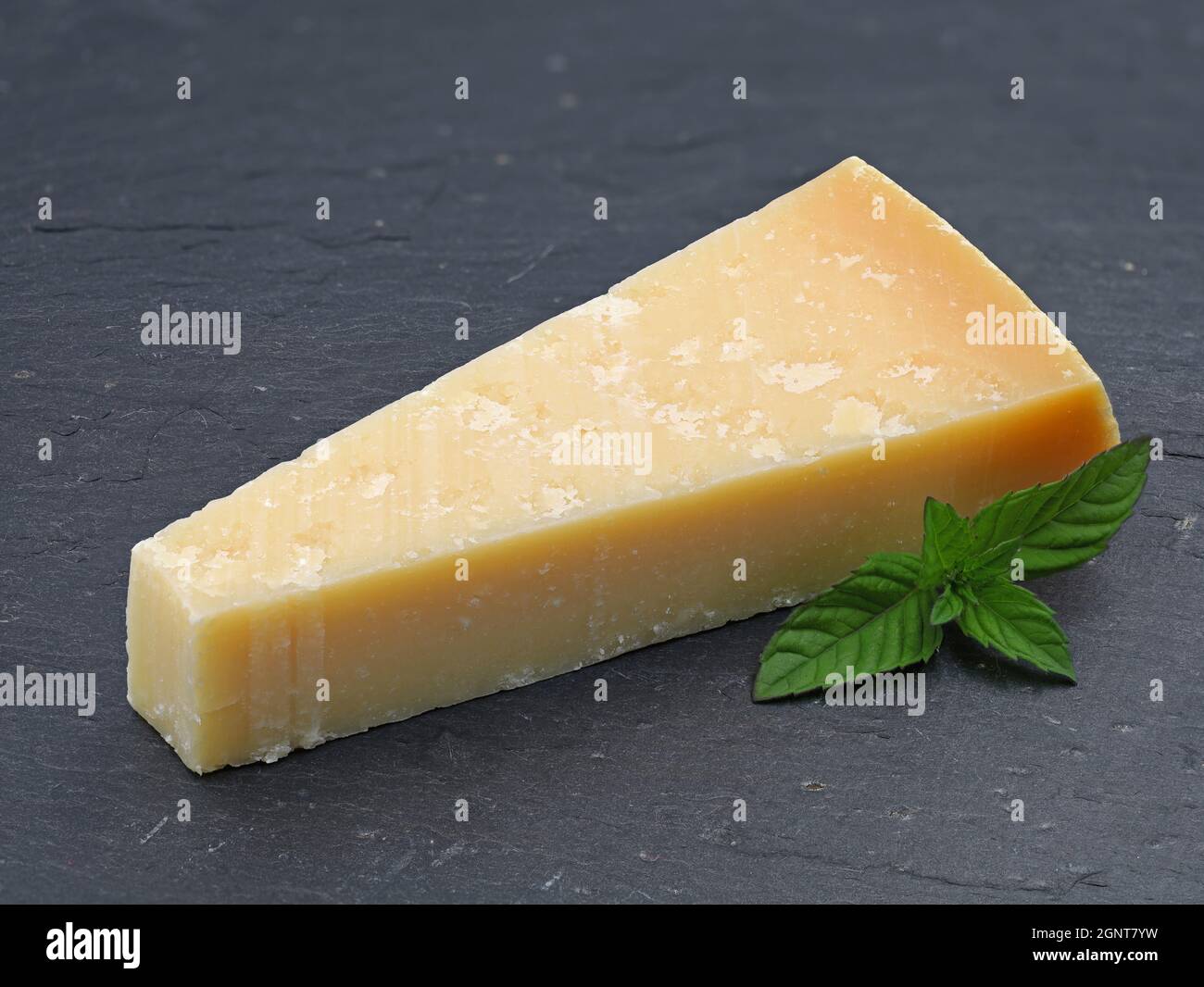 Ein Stück Parmigiano-Käse auf Schieferplatte, Parmesan mit grünem Blatt Stockfoto