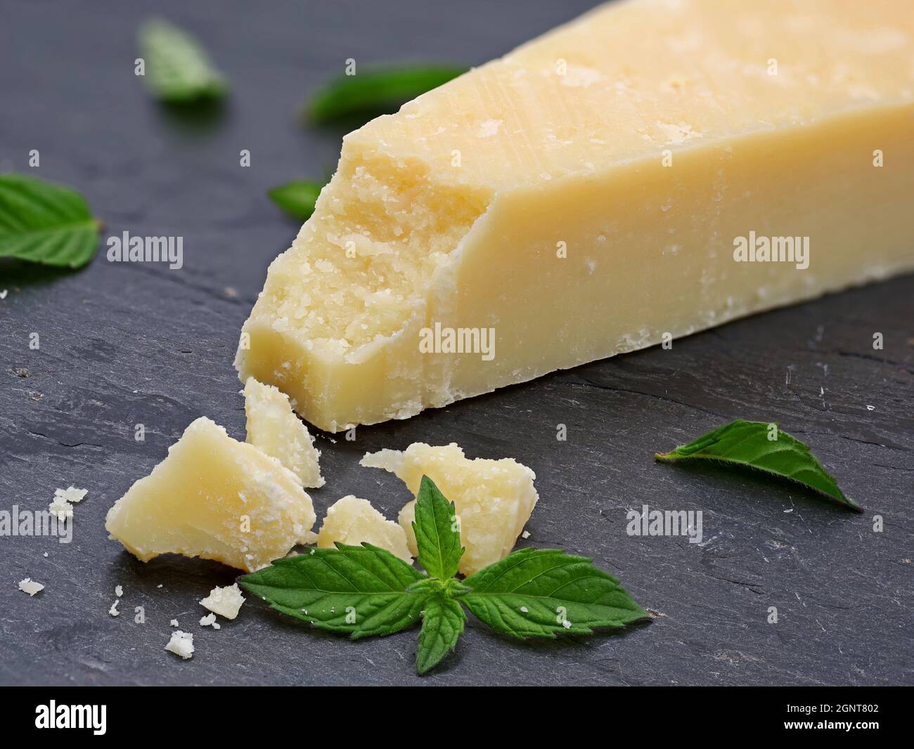 Stücke von köstlichem Parmesan-Käse auf dunklem Schieferteller mit grünen Minzblättern, Makroaufnahme von Parmigiano reggiano Stockfoto