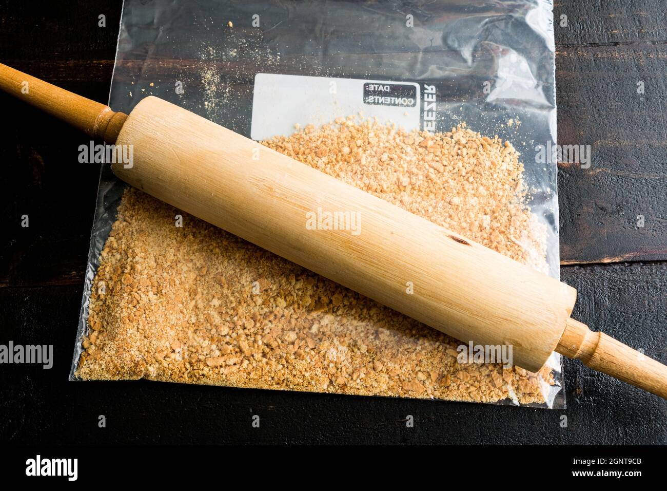 Graham Cracker Krümel mit einem Rolling Pin machen: Zerkleinerte graham Cracker in einem Plastikbeutel auf einem Holztisch Stockfoto