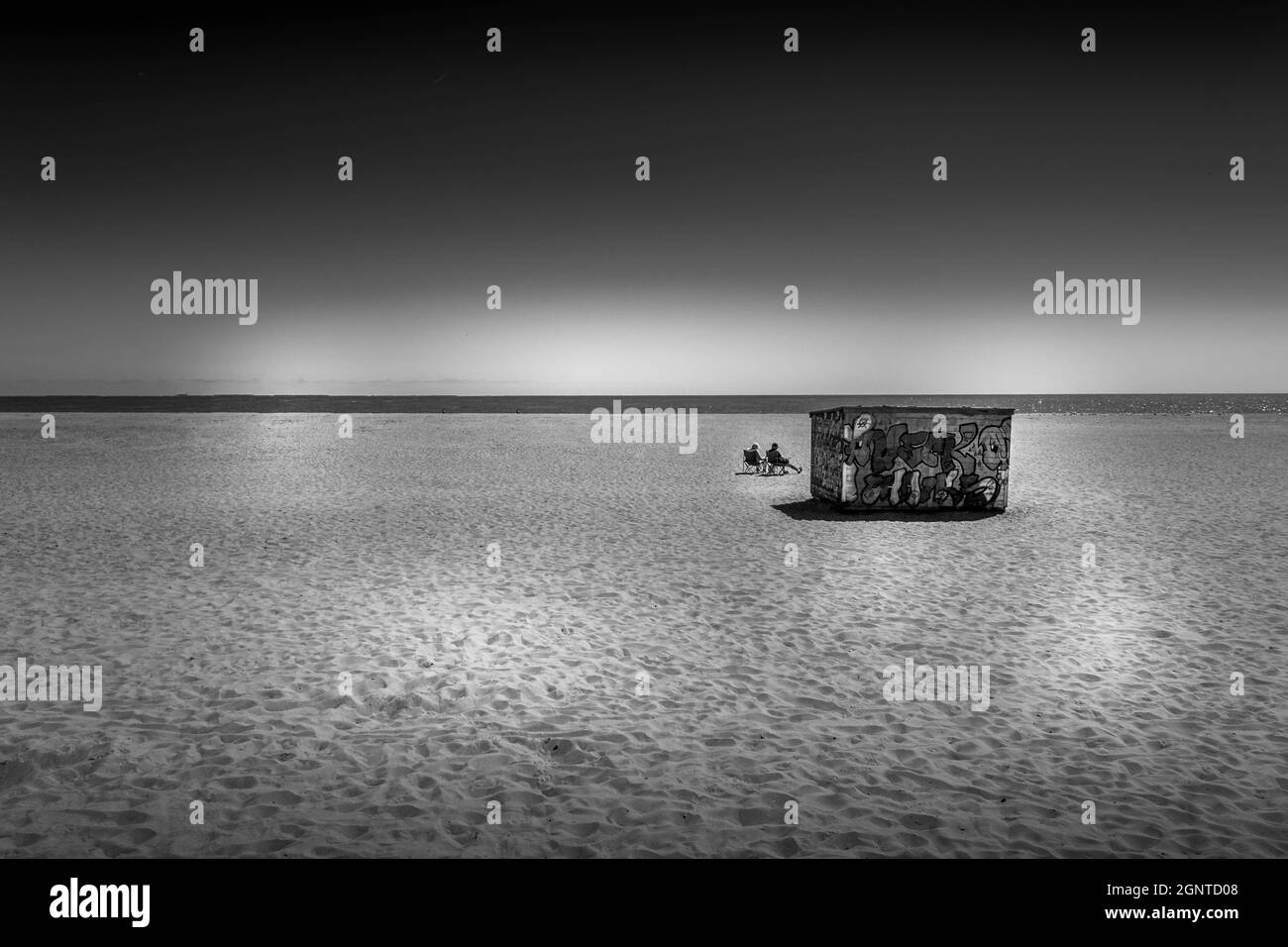 Monochrom-Bild von isolierten Paar am Strand, Great Yarmouth, Großbritannien. Mit Strand und Meer mit Graffiti Gebäude. Stockfoto