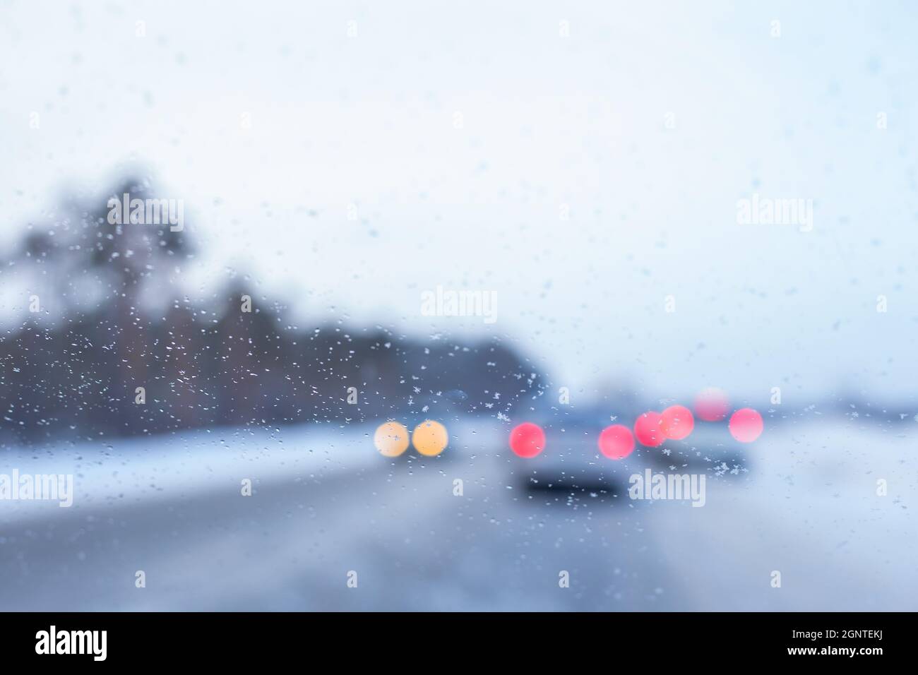 Verschwommener Hintergrund einer Windschutzscheibe mit Schneeflocken und Autos im Hintergrund Stockfoto