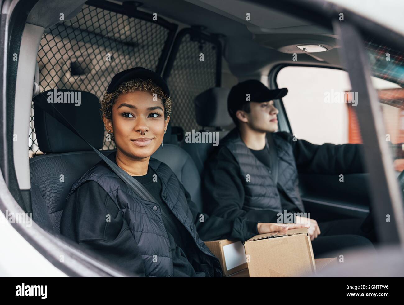 Zwei Lieferkollegen in Uniform sitzen zusammen in einem Lieferwagen. Eine Kurierin schaute aus dem Schaufensterwagen, während der Mann fuhr. Stockfoto